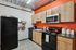 Chic modern kitchen with vibrant orange accent wall, sleek black appliances, and stylish wooden cabinetry.