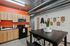 Modern kitchen with vibrant orange accent wall, sleek black appliances, and trendy industrial decor, featuring a stylish dining table with a potted plant centerpiece.