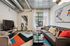 Modern living room with industrial charm, featuring a stylish gray sofa, colorful cushions, and eye-catching geometric rug. Natural light streams through large windows, highlighting the contemporary artwork and sleek metallic finishes.
