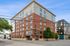 Contemporary mid-rise building with a blend of brick and modern design, located at a bustling city intersection, showcasing vibrant urban living.