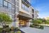 Elegant apartment entrance at Aston Place with modern architecture, lush landscaping, and inviting pathways under a clear blue sky.
