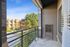 Charming apartment balcony with modern railing, offering views of lush trees and a nearby brick building under a clear blue sky.