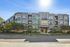 Modern apartment complex with a sleek exterior, large windows, and lush landscaping on a sunny day.