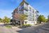 Modern apartment building with sleek design, large windows, and lush landscaping on a sunny street corner.
