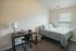 Bright and cozy bedroom featuring a comfortable bed, study desk with a sleek lamp, and natural light filtering through window blinds.