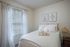 Charming bedroom with cozy bedding, elegant wall art, and soft natural light through sheer curtains.
