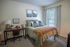 Cozy bedroom with stylish decor, featuring a comfortable bed with plush pillows, a modern desk with a lamp, and large window with elegant curtains.