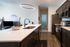 Modern kitchen with sleek dark cabinets, stainless steel appliances, and an elegant ring light fixture above the island.