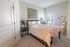 Warm and inviting bedroom with modern decor, featuring a cozy bed adorned with patterned bedding and a chunky knit throw. Natural light pours in through large windows, highlighting a charming bedside setup and artistic touches like a dreamcatcher and easel art.