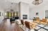 Bright and inviting modern living room featuring a central fireplace, elegant seating areas with leather chairs, and expansive windows offering a view of vibrant greenery.