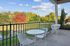 Charming balcony with modern white chairs and table, overlooking lush greenery and vibrant autumn trees.