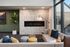 Luxurious living room with a modern fireplace, plush seating, vibrant cushions, and a large window offering natural light.