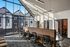 Bright, modern workspace with high ceilings and large windows offering natural light; sleek black chairs and a long wooden desk create an inviting, professional atmosphere.
