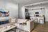 Modern open-plan living room and kitchen with sleek design, featuring a comfortable sofa, stylish artwork, and a high-end kitchen setup with bar seating.