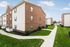 Charming brick apartment complex with well-maintained green lawns, inviting pathways, and bright windows under a clear blue sky.