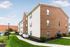 Charming brick apartment building with lush green lawns and a welcoming pathway under a clear blue sky.