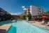 Luxurious apartment complex featuring a sparkling swimming pool with sun loungers, shaded seating areas, and modern architecture under a clear blue sky.