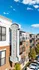 Elegant apartment building with modern brick facade, featuring private balconies and a charming vintage sign, under a vibrant blue sky.