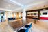 Modern communal area with ample natural light, featuring stylish wooden tables, navy blue seating, and vibrant red accents, perfect for co-working or social gatherings.