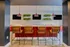 Modern kitchen bar with vibrant red accents, stylish pendant lighting, and lush greenery on white tiled walls.