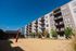 Modern apartment complex with private balconies overlooking a sandy volleyball court on a sunny day.