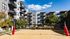 Modern apartment complex with stylish balconies and a vibrant sand volleyball court, set against a bright blue sky and lush greenery.