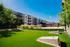 Modern apartment complex with stylish balconies and lush green courtyard, featuring a vibrant outdoor recreation area under a clear blue sky.