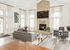 Bright, modern living space featuring a cozy stone fireplace, sleek gray sofas, and elegant decor accents with high ceilings and abundant natural light.