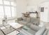 Bright, modern living room with large windows, cozy gray sofas, stylish coffee table, and an elegant open-plan kitchen.