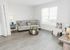 Bright, inviting living room with elegant gray sofa, accent chairs, and stylish decor, featuring modern wood flooring and a large window for natural light.