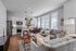 Bright and inviting open-concept living space featuring a modern kitchen with sleek white cabinets, a cozy living area with plush gray sofas, and large windows allowing ample natural light.