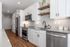 Modern kitchen with sleek stainless steel appliances, chic white cabinetry, and elegant open shelving on warm wood flooring.