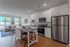 Modern open-concept kitchen and living area with sleek white cabinetry, stainless steel appliances, and large sunlit windows.