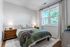 Inviting bedroom with elegant decor, featuring a cozy bed with a green quilt, dual bedside lamps, and a large window letting in natural light.