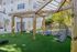 Charming outdoor space featuring stylish hanging chairs under a wooden pergola, surrounded by lush greenery and well-maintained grounds.