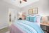 Charming bedroom with soft pastel bedding, stylish d&eacute;cor, and an inviting workspace, leading to an open walk-in closet and modern bathroom.