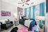 Vibrant bedroom with bold artwork, plush black chair, and teal curtains, featuring chic decor and ample natural light.
