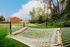 Relaxing outdoor space featuring rows of hammocks on a lush green lawn, surrounded by serene trees and modern housing.