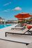 Elegant poolside setting with vibrant orange umbrellas and plush loungers, perfect for relaxing days under a clear blue sky.