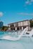 Luxurious apartment complex showcasing a modern building with expansive windows and a pristine outdoor pool featuring elegant lounge chairs, set against a clear blue sky.