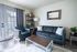 Inviting living room with modern dark leather couch, cozy armchair, and large window for natural light.