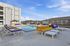 Inviting apartment pool area with vibrant yellow and purple loungers, modern white tables, and sunlit gazebo.