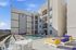 Modern apartment complex with a vibrant pool area featuring colorful lounge chairs and seating against a bright blue sky, offering a luxurious and inviting outdoor experience.