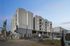 Modern apartment complex with multi-story design, ample balconies, and secure gated parking under a clear blue sky.