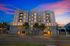 Elegant modern apartment building at sunset featuring large windows, palm trees, and inviting lighting, perfect for urban living.