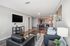 Modern open-concept living room with sleek black furniture, stylish kitchen, and cozy dining area, ideal for sophisticated apartment living.