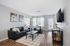 Inviting living room with modern decor, featuring a sleek black leather sofa, cozy armchair, stylish coffee table, framed artwork, and natural light streaming through large windows.