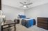 Cozy bedroom with modern decor, featuring a comfortable bed with plush blue bedding, a sleek ceiling fan, and a stylish desk setup for productivity.