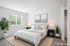 Elegantly staged bedroom with a cozy bed, stylish side tables, indoor plants, and large window providing natural light.