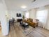 Bright and spacious living room featuring a stylish tan sofa, elegant area rug, modern TV setup, and chic bar seating in an open-concept apartment.